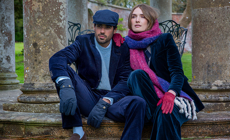 Woman wearing a scarf and suede gloves sat with a man wearing waxed cotton gloves and a flat cap at a country estate