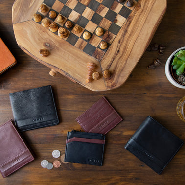 Men's various leather wallets in brown and black on a coffee table with a chessboard