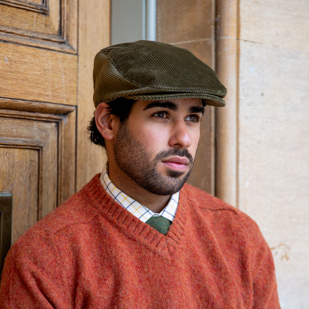 Man wearing a corduroy flat cap and orange jumper stood by a wooden door