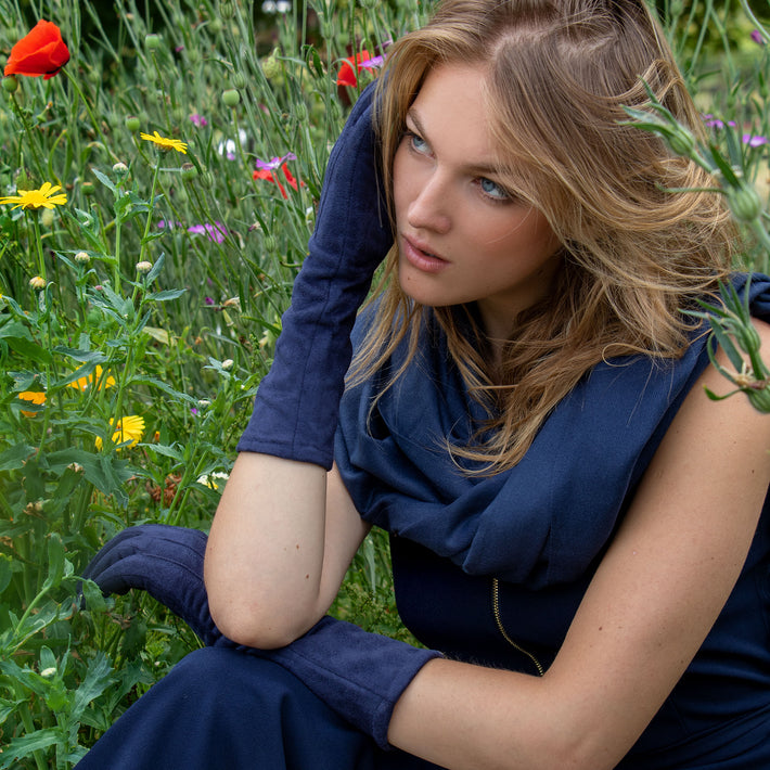 Woman wearing long navy blue faux suede gloves and blue dress in a flowery meadow