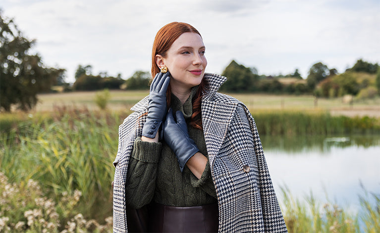 Woman wearing leather gloves with three buttons in navy walking around a meadow