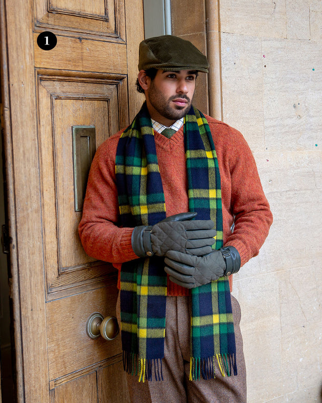 Man wearing touchscreen water resistant olive leather gloves with waxed cotton quilting, wearing a plaid scarf and corduroy hat by a grand door