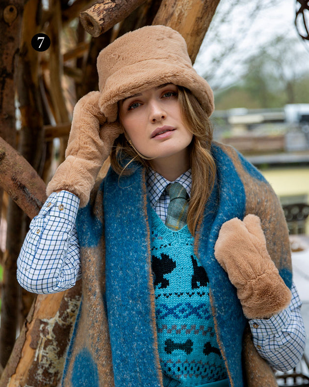 A woman wearing womens faux fur bucket hat in camel with matching mittens and a blanket scarf in the park