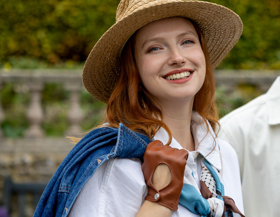 Woman wearing a straw hat and leather driving gloves in cognac outdoors