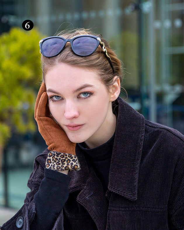 Woman wearing touchscreen velour lined faux suede gloves with faux fur leopard print cuffs in cognac in a cafe