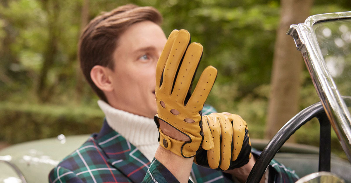 Man wearing yellow leather gloves in a vintage car with a forest background