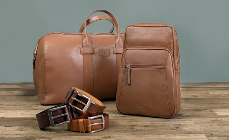 Two men's brown leather bags and three men's brown leather belts positioned on the floor.