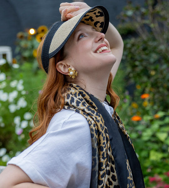Woman wearing summer straw visor with leopard print pattern sitting on a park bench