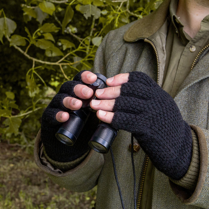 Man wearing fingerless knitted gloves in black holding binoculars for shooting