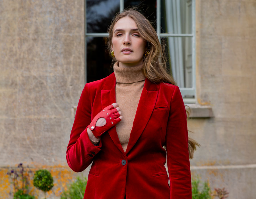 Woman wearing red fingerless leather gloves with red velvet suit, outside in the garden. 