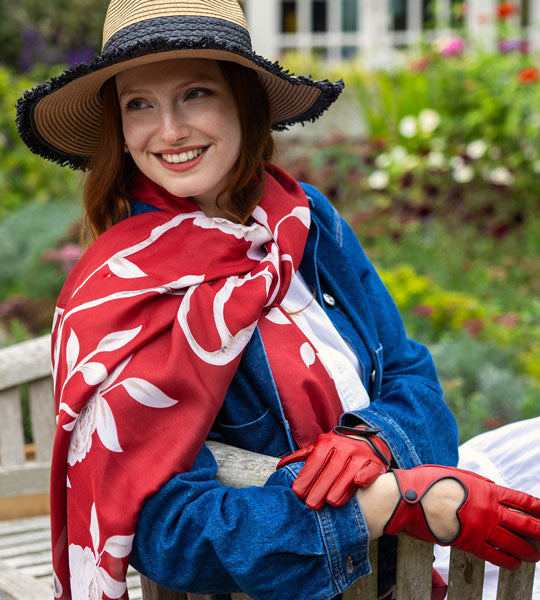Woman wearing red satin scarf with red gloves and straw hat in the garden.